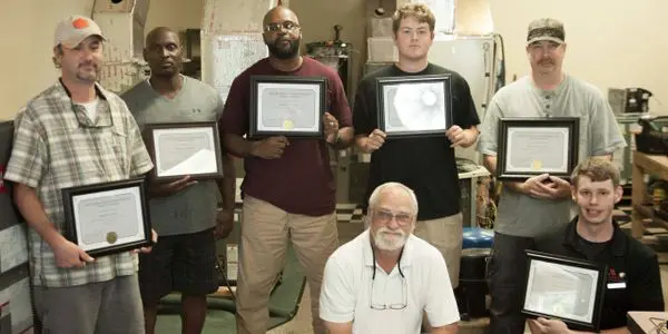 A group of men holding up framed drawings.