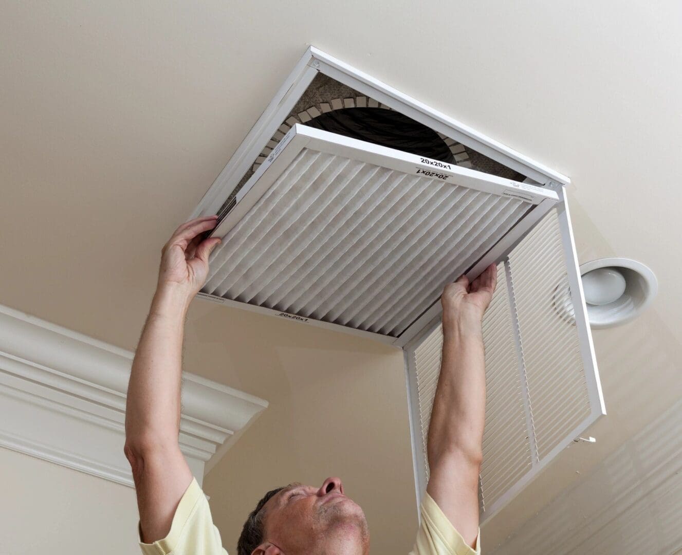 A man is holding an air filter up to the ceiling.